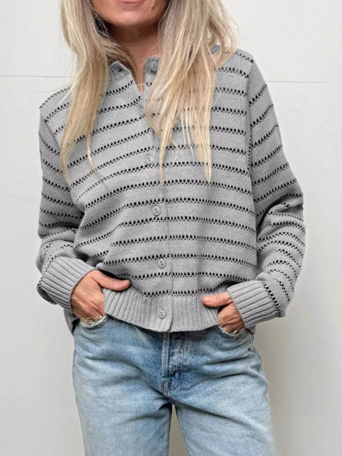 A woman wears a gray striped button-up cardigan sweater and light wash jeans.