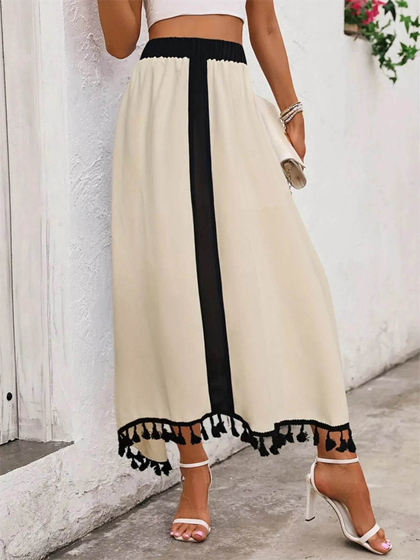 A model wears a high-waisted, cream-colored skirt with a black vertical stripe and tassel trim.