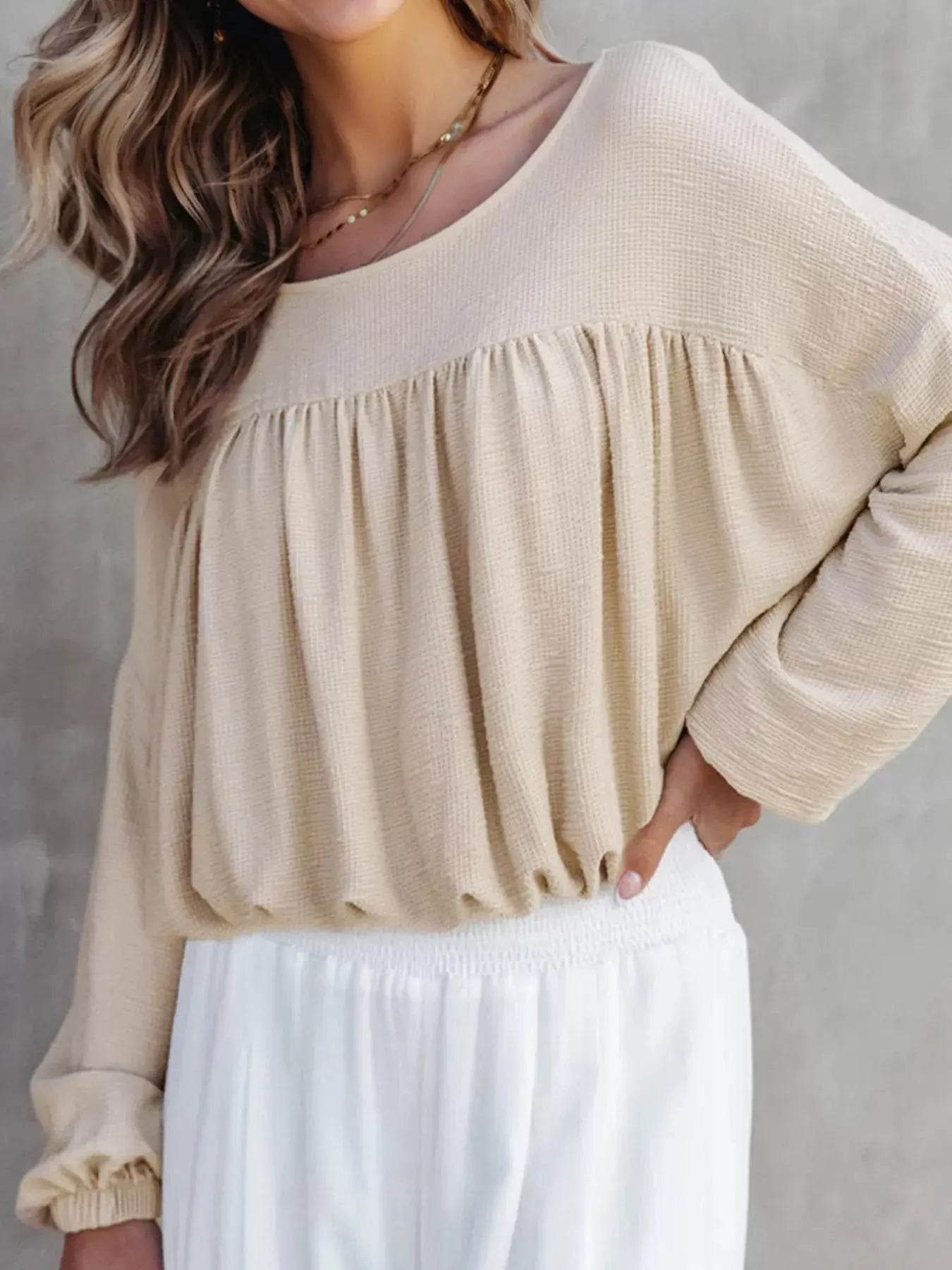 A woman wears a beige textured drop shoulder long sleeve top with white pants.