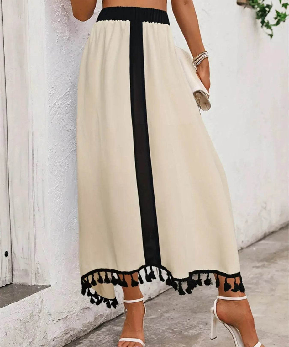 A model wears a high-waisted, cream-colored skirt with a black vertical stripe and tassel trim.