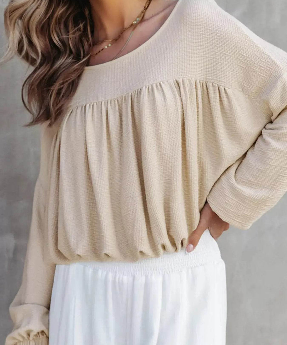 A woman wears a beige textured drop shoulder long sleeve top with white pants.
